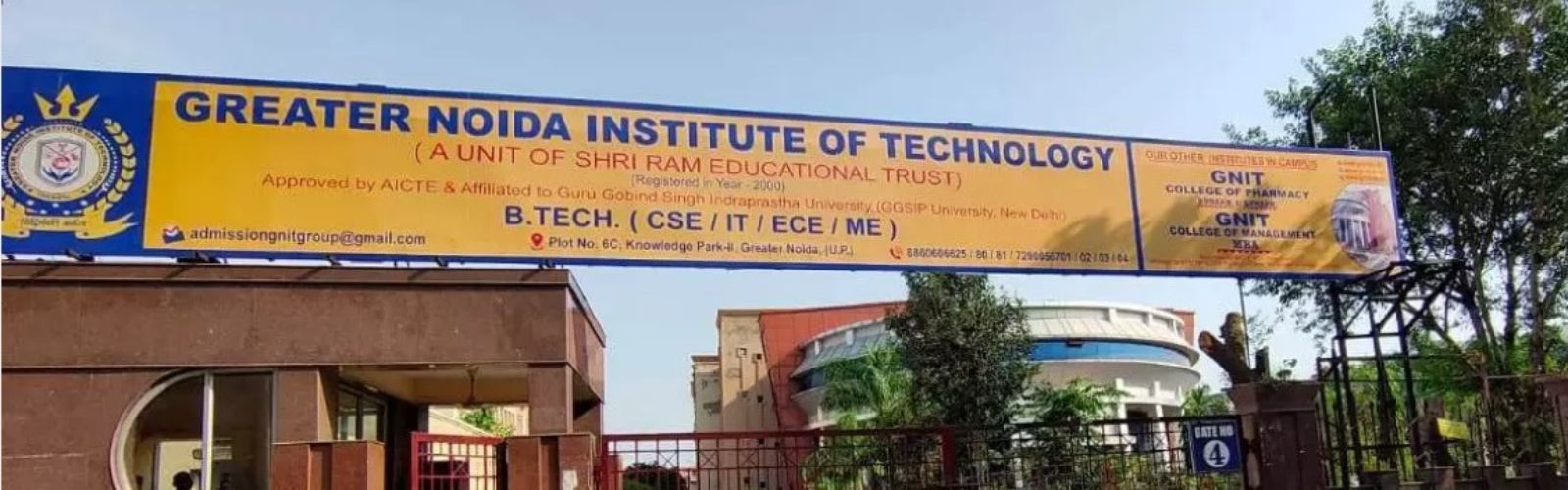 A modern circular academic building of GN Group of Institutes on a sunny day. A yellow sign is above the glass door, with a large park, red benches, and students in the foreground.