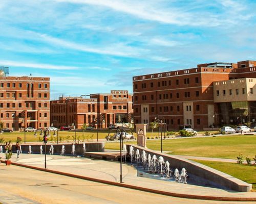 Alt Text: Wide aerial view of JECRC University Jaipur campus featuring modern red-brick academic buildings, green lawns, and a central fountain under a blue sky.