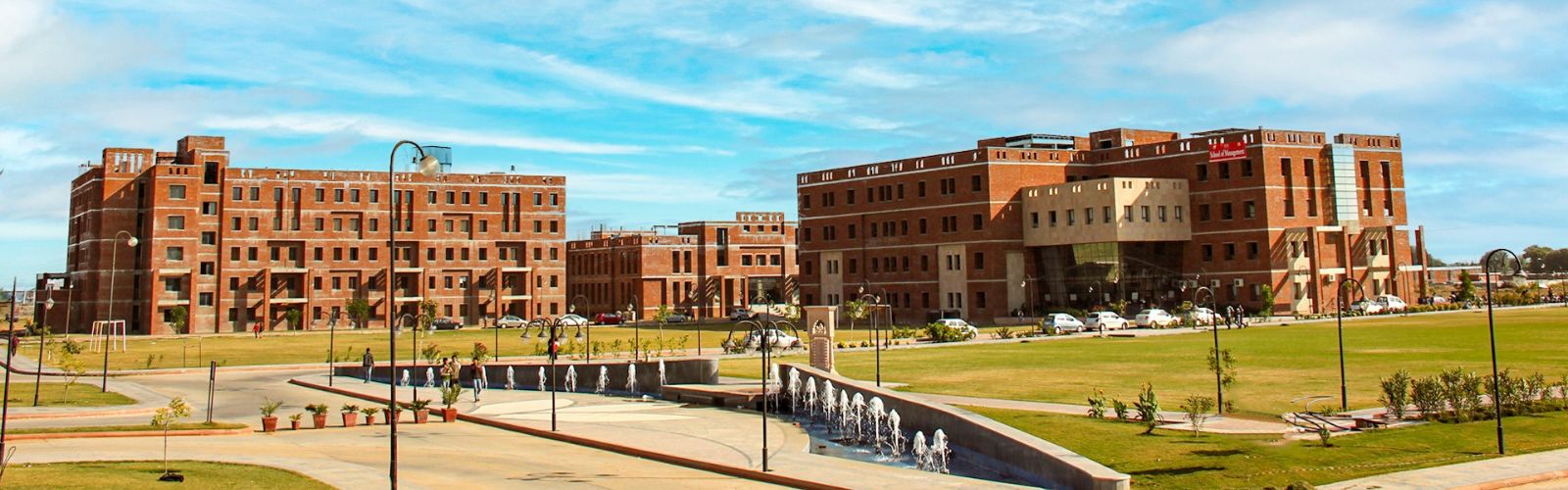 Alt Text: Wide aerial view of JECRC University Jaipur campus featuring modern red-brick academic buildings, green lawns, and a central fountain under a blue sky.